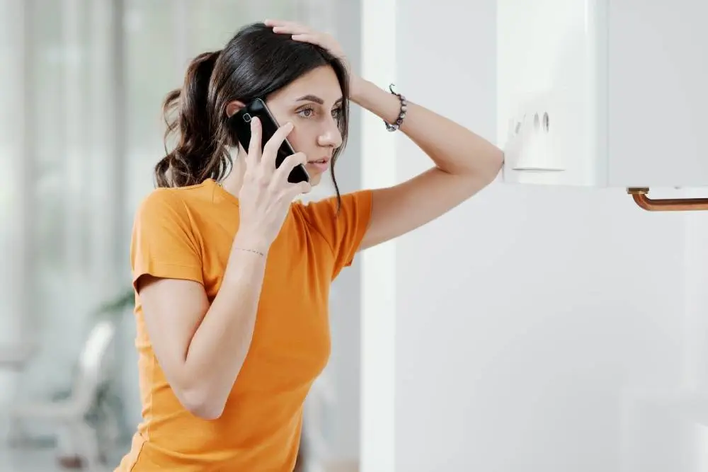 A woman calls a service technician while standing near her furnace.